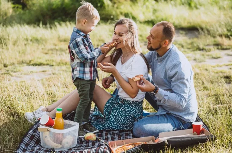 family-having-picnic-eating-pizza-park-907x600